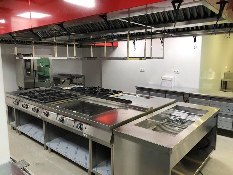 Linea di cottura in acciaio inox sotto una cappa aspirante rossa