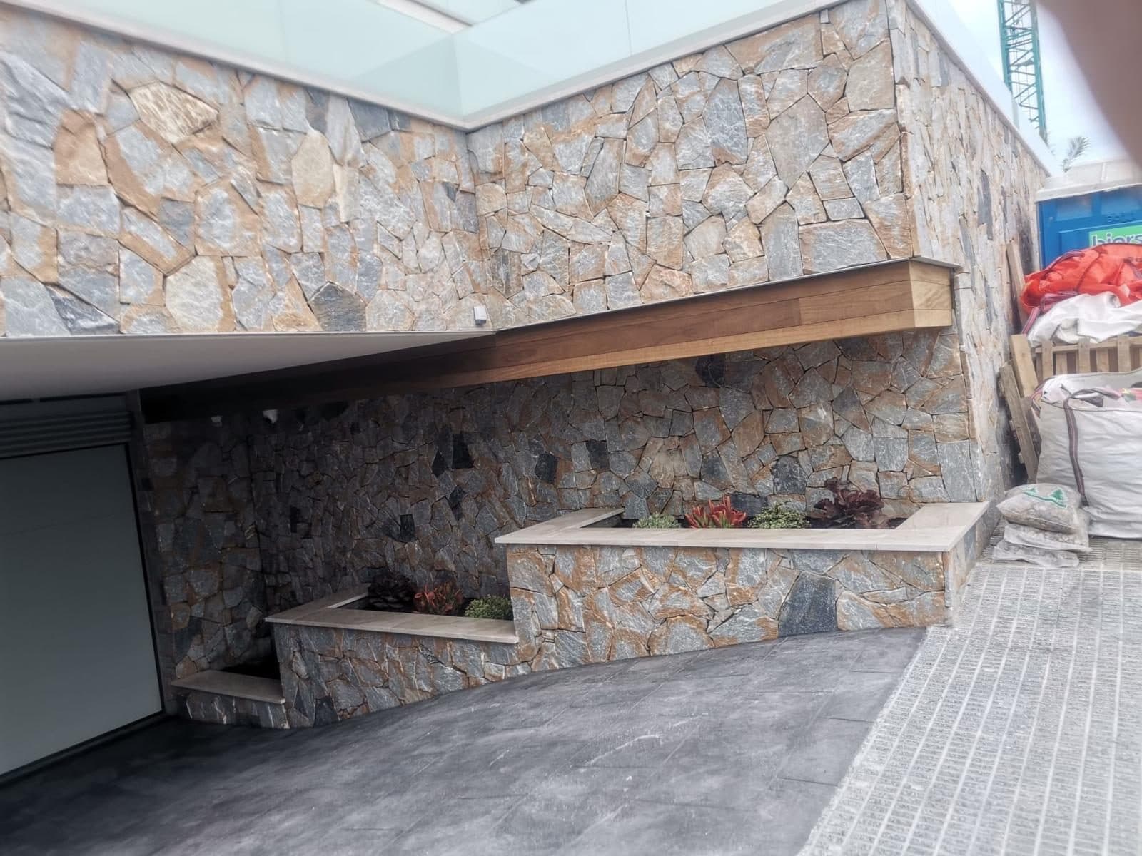 Überdachte Terrasse mit Natursteinverkleidung und eingebauten Pflanzkübeln